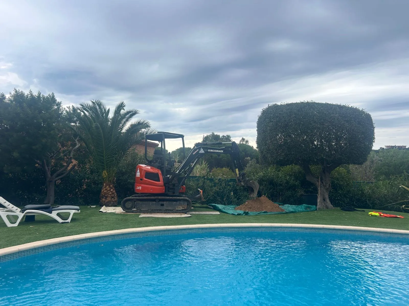 Mini-pelle dans un jardin, au bord d’une piscine