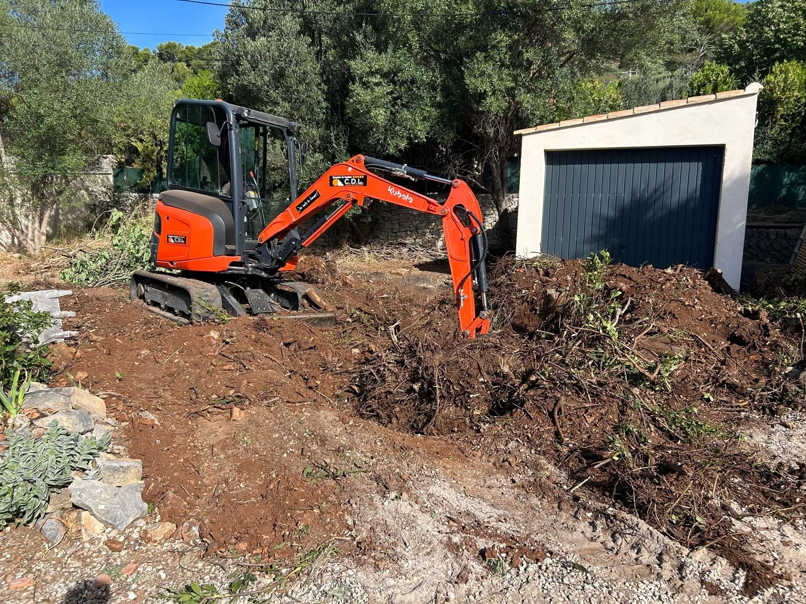 Mini-pelle en train de terrasser un terrain devant un garage